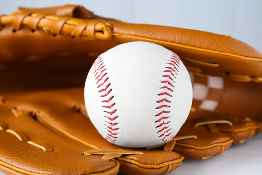 Leather baseball glove with ball on white wooden table, closeup