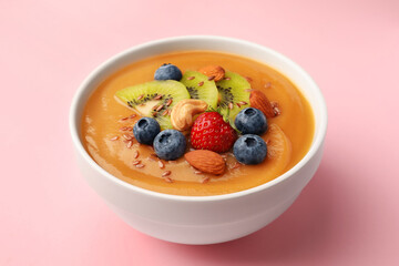 Delicious smoothie bowl with fresh berries, kiwi and nuts on pale pink background