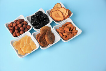 Bowls with dried fruits and nuts on light blue background, space for text