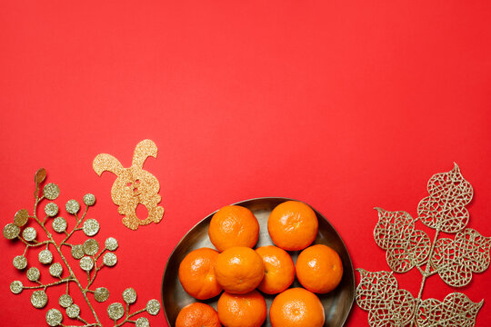 Chinese or lunar new year flat lay with plate of mandarins, paper rabbit as symbol of 2023 and golden flowers on red