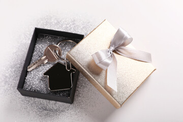 Key with trinket in shape of house, glitter and gift box on light grey background. Housewarming party