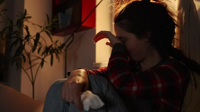 Psychology disorder and loss. Portrait of suffering crying young Caucasian woman sitting on sofa in home. Concept of depression and despair.