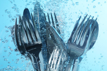 Washing silver cutlery in water on light blue background