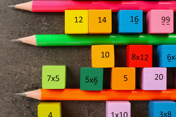 Many colorful cubes with numbers, multiplications and pencils on dark grey table, flat lay