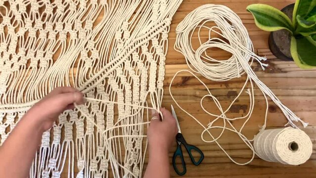 A young woman hand crafting a Macrame wall hanging on a wooden background 