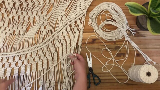 A young woman hand crafting a Macrame wall hanging on a wooden background 