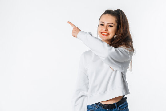 Look at this. Cheerful lovely brunette woman pointing at upper left corner with beaming smile, looking pleased, satisfied with good offer, standing against white studio background