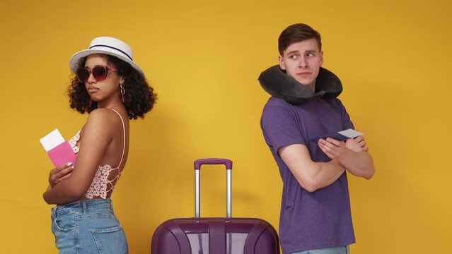Journey disagreement. Aggrieved couple. Bad vacation. Displeased man and woman staying back each other with baggage and documents on yellow background.
