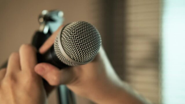 Close-up of a musician hand picking up a microphone for singing. put it on the mic stand. at home studio practice.