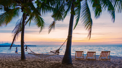 Hammock and beach chairs on the beach with palm trees during sunset at Na Jomtien Beach Pattaya Thailand.