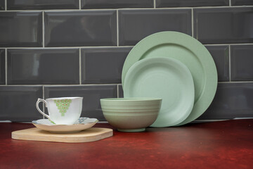 breakfast dinner service of bone china cup and saucer with green plate, side plate and bowl on red worktop and grey splash back tiles