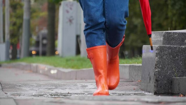 Woman in bright orange rain boots walking towards camera in city, closeup