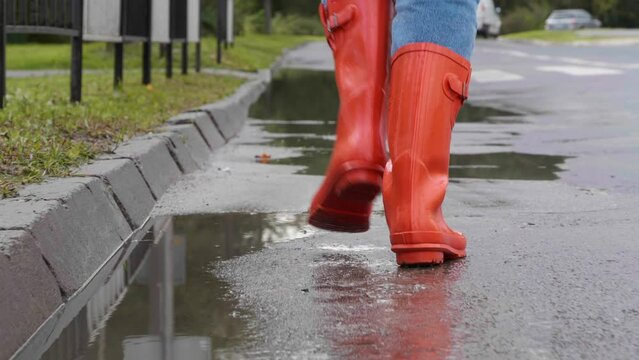 Woman in bright orange rain boots running outdoors, back closeup view. Camera following after her