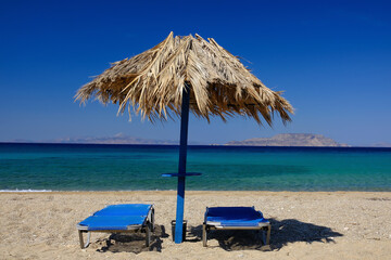 Two sun beds and a sun umbrella at the amazing beach of Agia Theodoti in Ios Greece