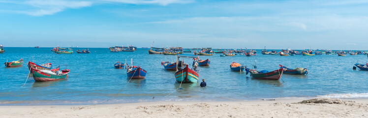 Fototapeta na wymiar Panorama white sandy beach, calm waves with traditional wooden fishing boat anchored near shoreline in sunny cloud blue sky at Bai Truoc, Vung Tau, Vietnam