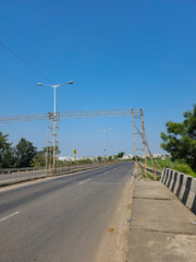 Stock photo of empty asphalt road surrounded by green plants and trees, LED street lamps or light in the middle of the road, blue sky on background. Picture captured under bright sunlight at Gulbarga.