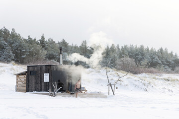 Wooden outdoor sauna with a smoke coming out of chimney on a beautiful cold snowy winter day at the Baltic sea. Well being and healthy life style.