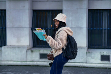 Young african american student on a winter break exploring new city, she's trying to find tourist attractions using her map and tourist guide as she walks in a big city