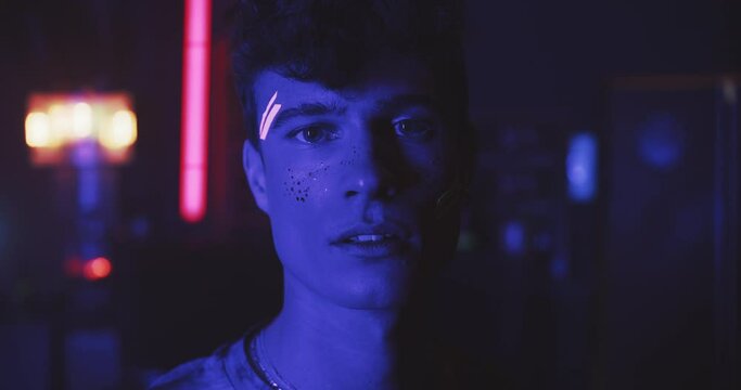 Person with neon and glitter make up looks toward the camera 