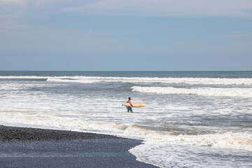 BALI, INDONESIA - NOVEMBER 10, 2022: Male surfer with surfboard spending sunny day on beach near...