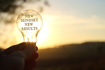 Fototapeta Hand holding light bulb with the text new mindset in front of the bright sun obraz