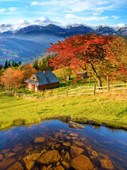 breathtaking view with stones in the pond and hut in the autumn mountains against the background of snow-capped peaks.