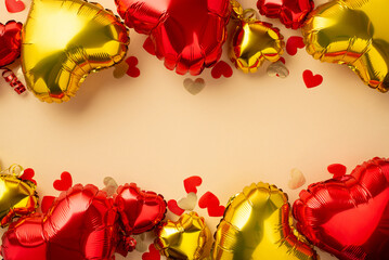 Saint Valentine's Day concept. Top view photo of heart shaped confetti red and golden balloons on isolated pastel beige background with blank space in the middle