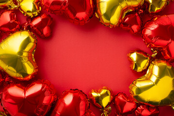 Valentine's Day concept. Top view photo of heart shaped red and golden balloons on isolated red background with copyspace in the middle