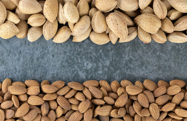 Frame of heap of peeled almonds and almonds in shell on gray background. Top view. Copy Space.