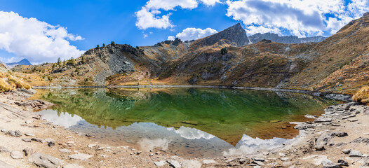 Alpine mountain peaks covered with sparse autumn vegetation and white clouds in the blue sky are...