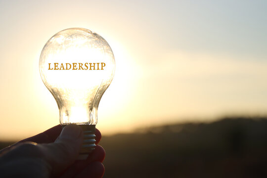 Hand holding light bulb with the text leadership in front of the bright sun