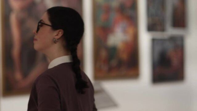Side view portrait of young pretty Caucasian woman wearing eyeglasses take photo with smartphone in art exhibition. Visiting excursion in museum. Concept of educational and cultural tourism.