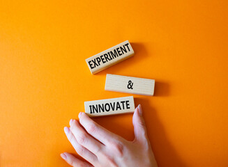 Experiment and innovate symbol. Concept words Experiment and innovate on wooden blocks. Businessman hand. Beautiful orange background. Business and Experiment and innovate concept. Copy space.