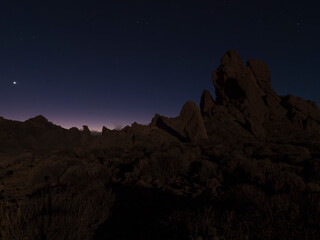 Fototapeta na wymiar Long exposure night shot of Roques de Garcia volcanic rock formation at El Teide national park, early night winter sky with stars on pink blue glow. Tenerife Canary islands, Spain