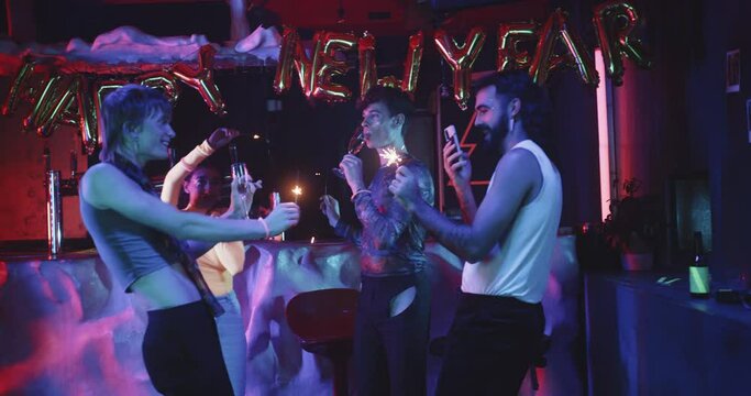 Group of friends dance together in a club with sparklers 