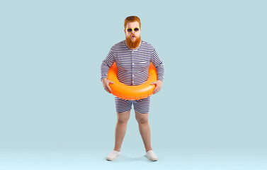 Funny chubby male swimmer with inflatable swimming circle looks at camera in shock on pastel light...