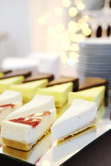 Cheesecakes on a mirror tray stand on a buffet table against the background of golden bokeh