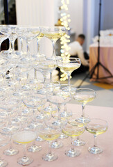Pyramid of empty and filled with champagne glasses against the backdrop of the interior of the hall.