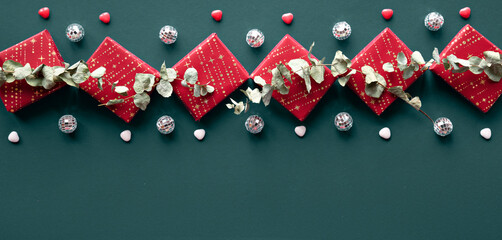 Wintertime green red decorative border with gift boxes, disco balls and eucalyptus. Flat lay on...