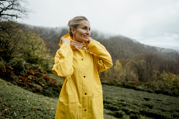 Pretty woman in yellow raincoat walking in rainy weather in the countryside © Ilona