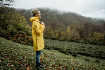 Middle aged woman in yellow raincoat walking in rainy weather in the countryside © Ilona