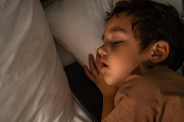 Fototapeta na wymiar Little sleeping boy on the bed with a phone. 