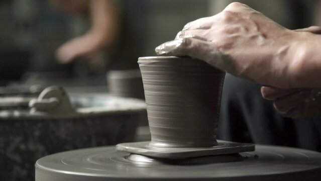 Gental hand and fingers building clay spindle shaping pottery design on wheel by professional potter artist.