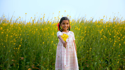 Portrait of a little village girl happily showing a bunch of beautiful yellow flowers - Indian...