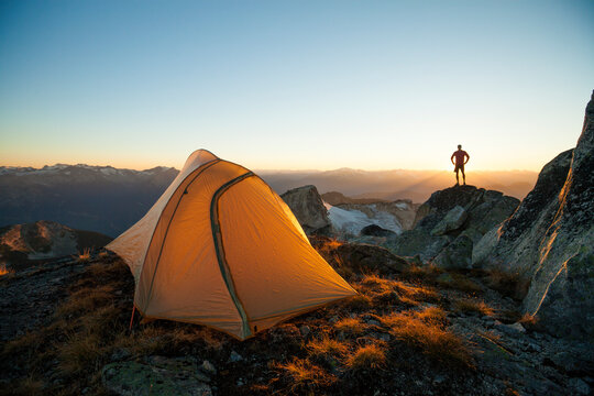 A silhouetted hiker stands on a rock bluff while camping on Saxifrage Peak, Pemberton, BC, Canada.