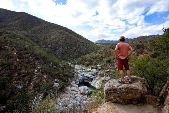 A man overlooks a steep valley and a waterfall in the desert.