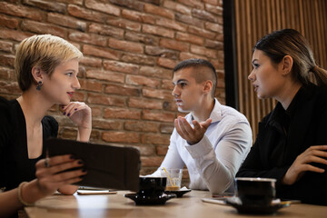 Three young business colleagues having a meeting in a modern cafe in the late evening hours. Successfull startup team analysing data after work hours.