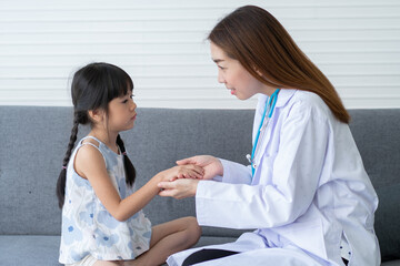 Asian woman pediatrician doctor hold stethoscope for exam a little girl patient and heck heart lungs of kid, Good family doctor visiting child at home, Healthcare and medicine for childhood concept.