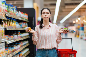 Young caucasian woman holds products in hands and can't do choice. Concept of shopping in...