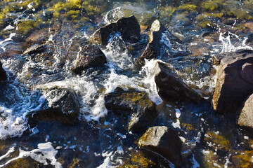 Sea waves crash against the rocks in the sea and create white foam. Top view of sea waves crashing the rocks in the Aegean sea